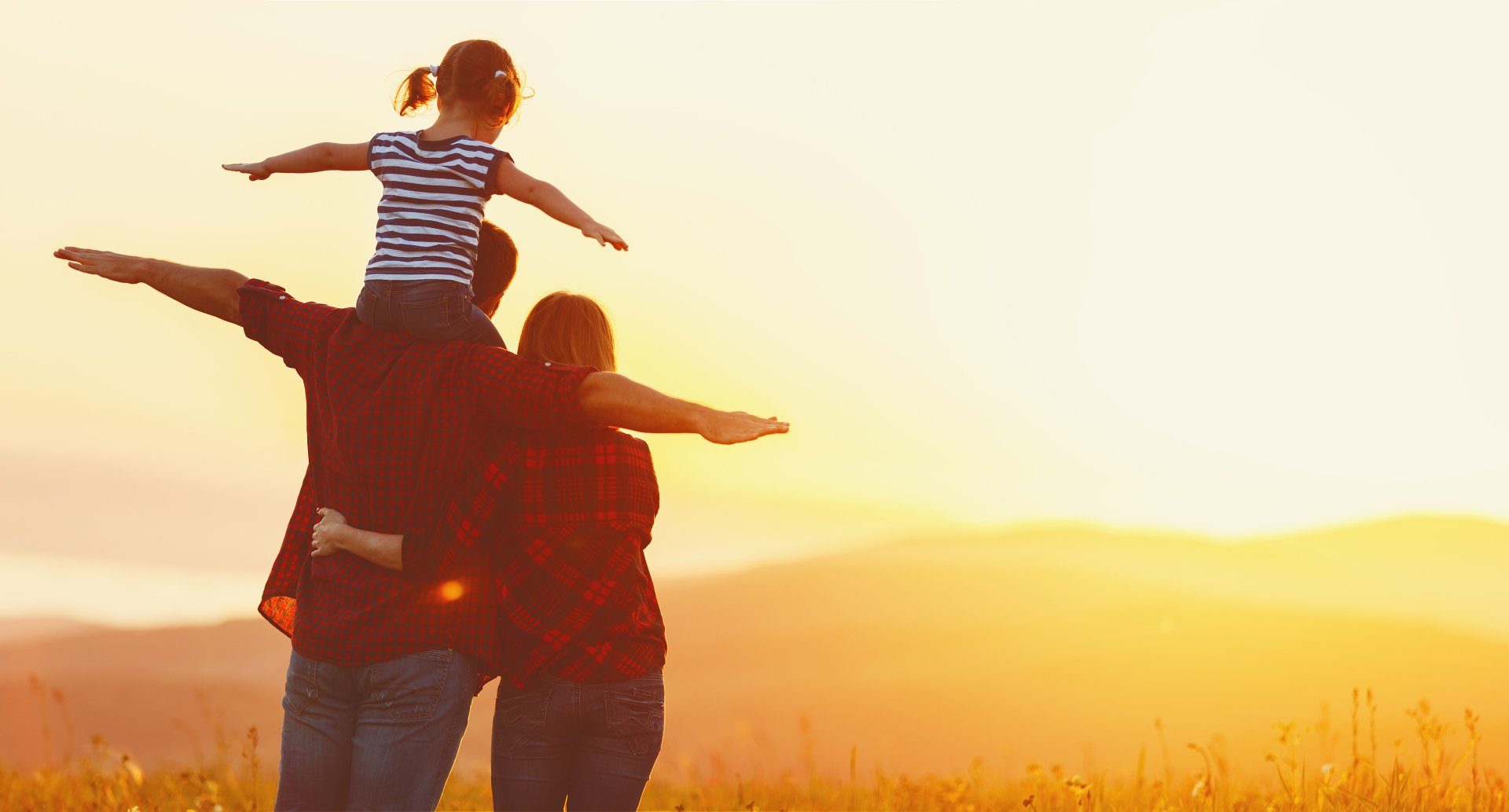 A parent lifting a child overhead, silhouetted against a sunset