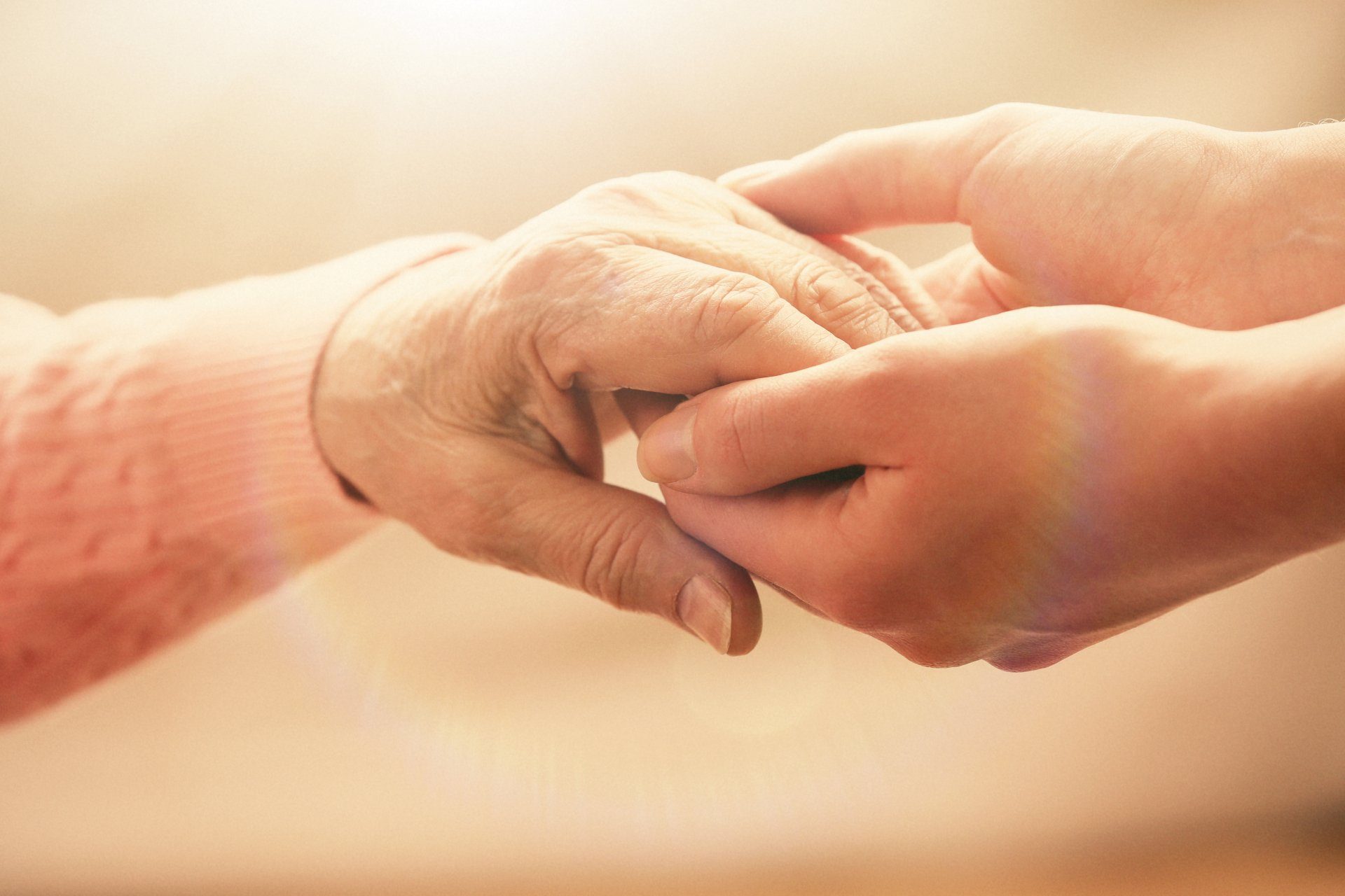 A younger hand gently holding an older person’s hand