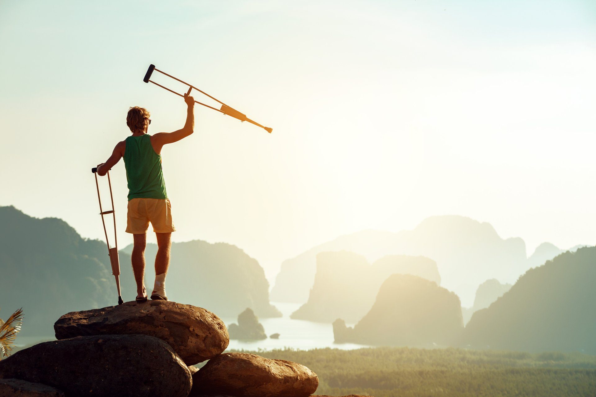 A hiker on a rock outcrop raising a walking stick against a sunrise